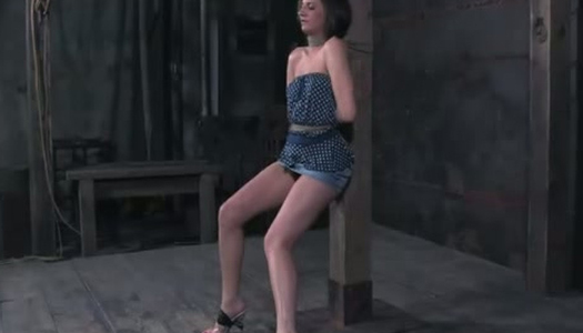 Pornobild An eine Stange gefesselt wird Brünette im dunklen Raum bestraft